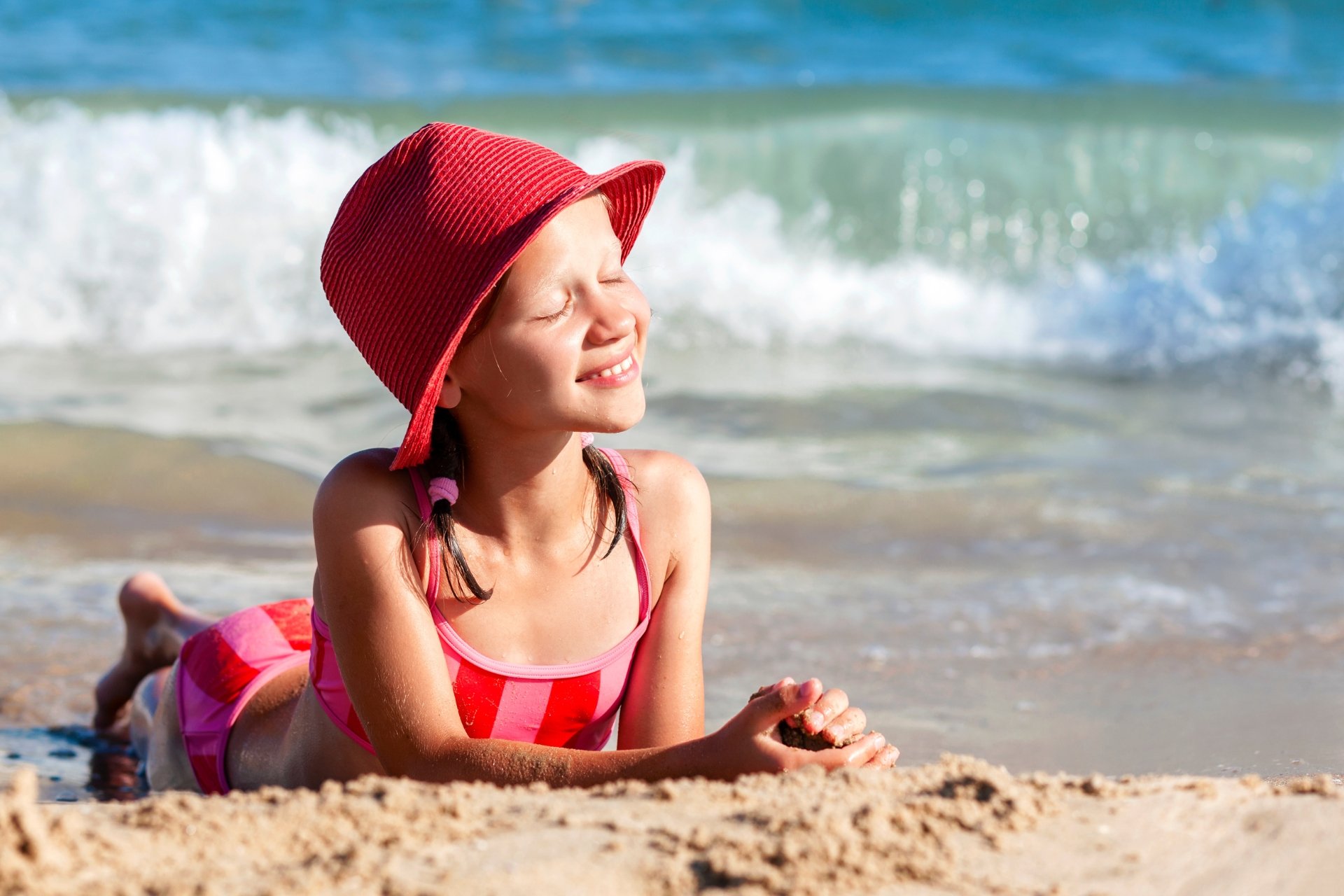 Bambina sdraiata sulla sabbia in riva al mare
